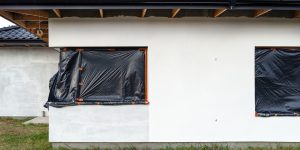 A newly applied layer of white silicone plaster on the wall of the house, the corner window is prote